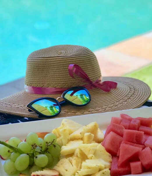 sun hat, platter of freshly cut fruit next to pool